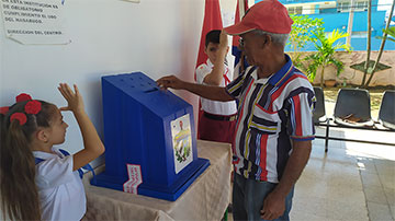 Elector introdujo boleta de votación en una urna custodiada por dos pioneros