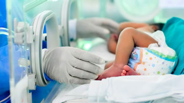Incubadora con bebé y manos de atención médica